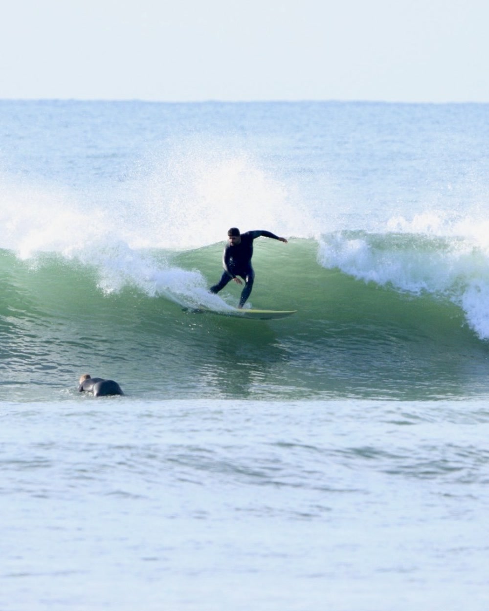 Surfer on a clean green wave at Jeffreys Bay with another surfer paddling on the inside