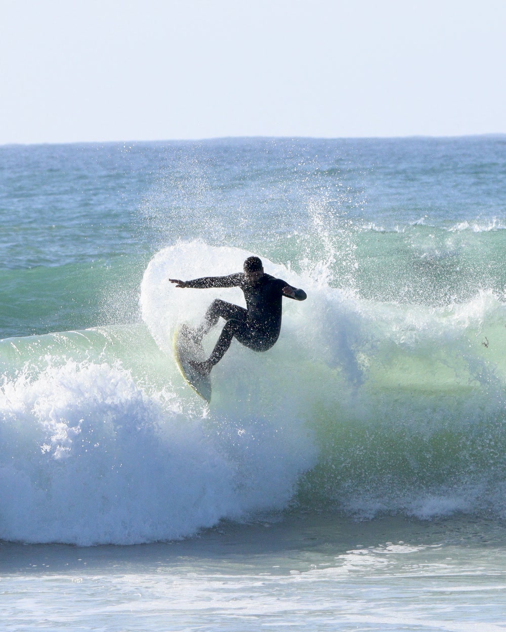 Surfer driving hard off the top of a green wave at Jeffreys Bay, spray flying