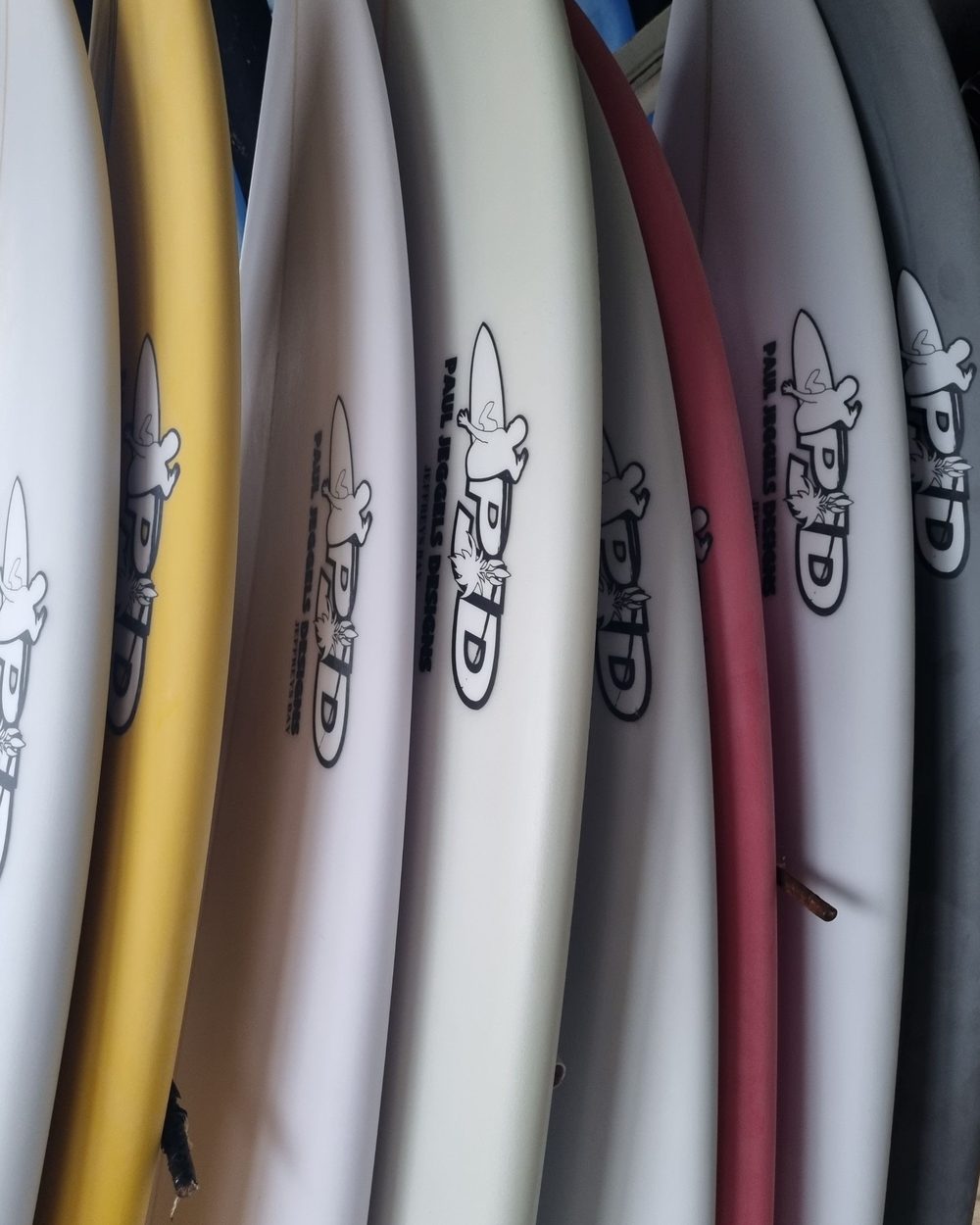 A close rack of finished surfboards seen along their rails, the Paul Jeggels Designs logos visible down the row