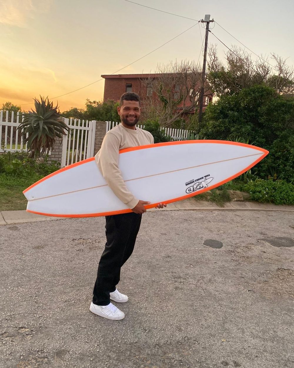 Daniel Jeggels at sunset in Jeffreys Bay holding his custom surfboard by Paul Jeggels Designs