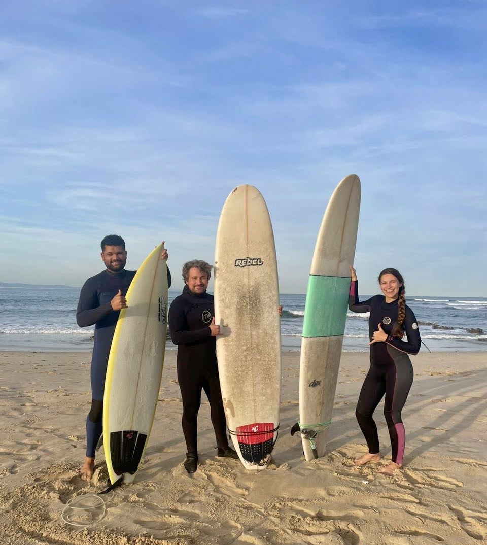 Three surfers in wetsuits on the beach at Jeffreys Bay holding their surfboards after a session